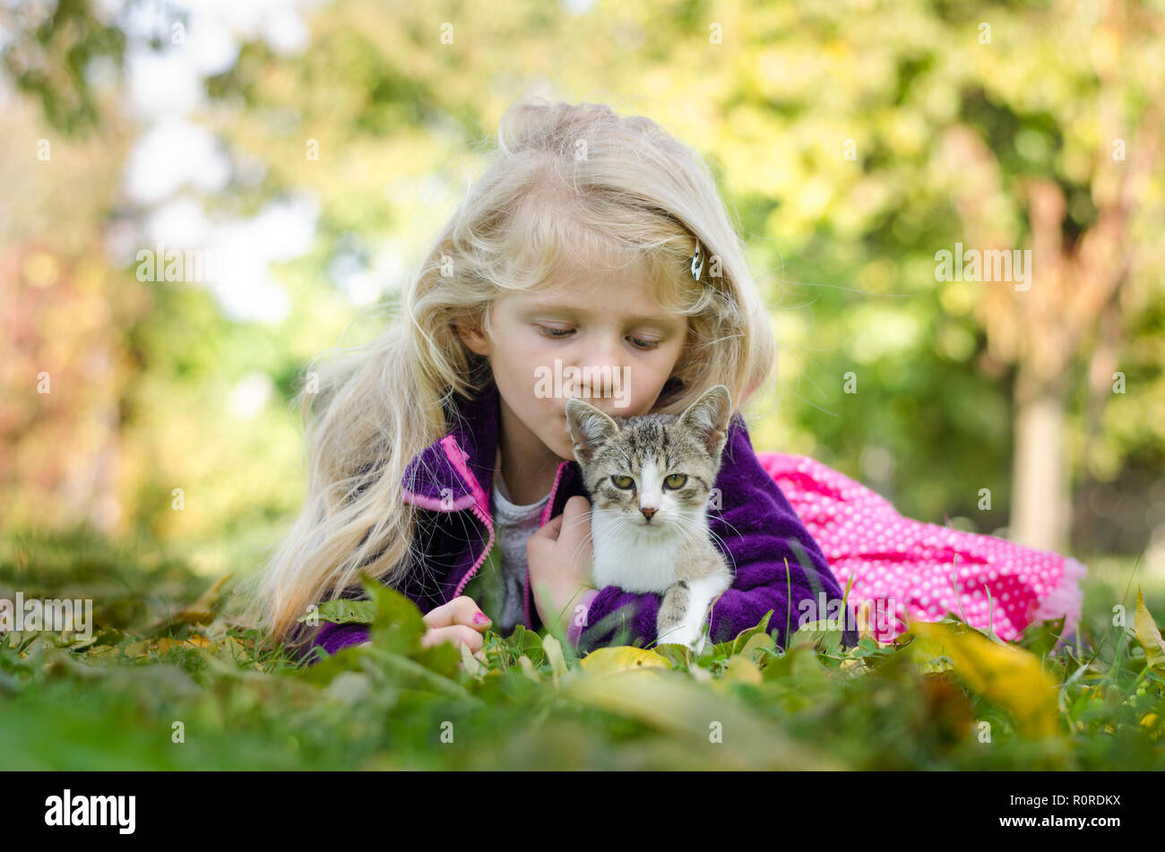 Schöne blonde Mädchen mit Katze und zusammen liegen auf Gras im Herbst Stockfoto