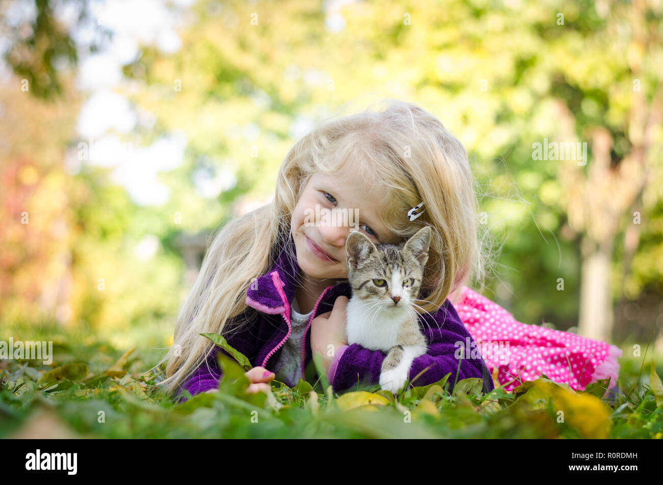 Schöne blonde Mädchen mit Katze und zusammen liegen auf Gras im Herbst Stockfoto