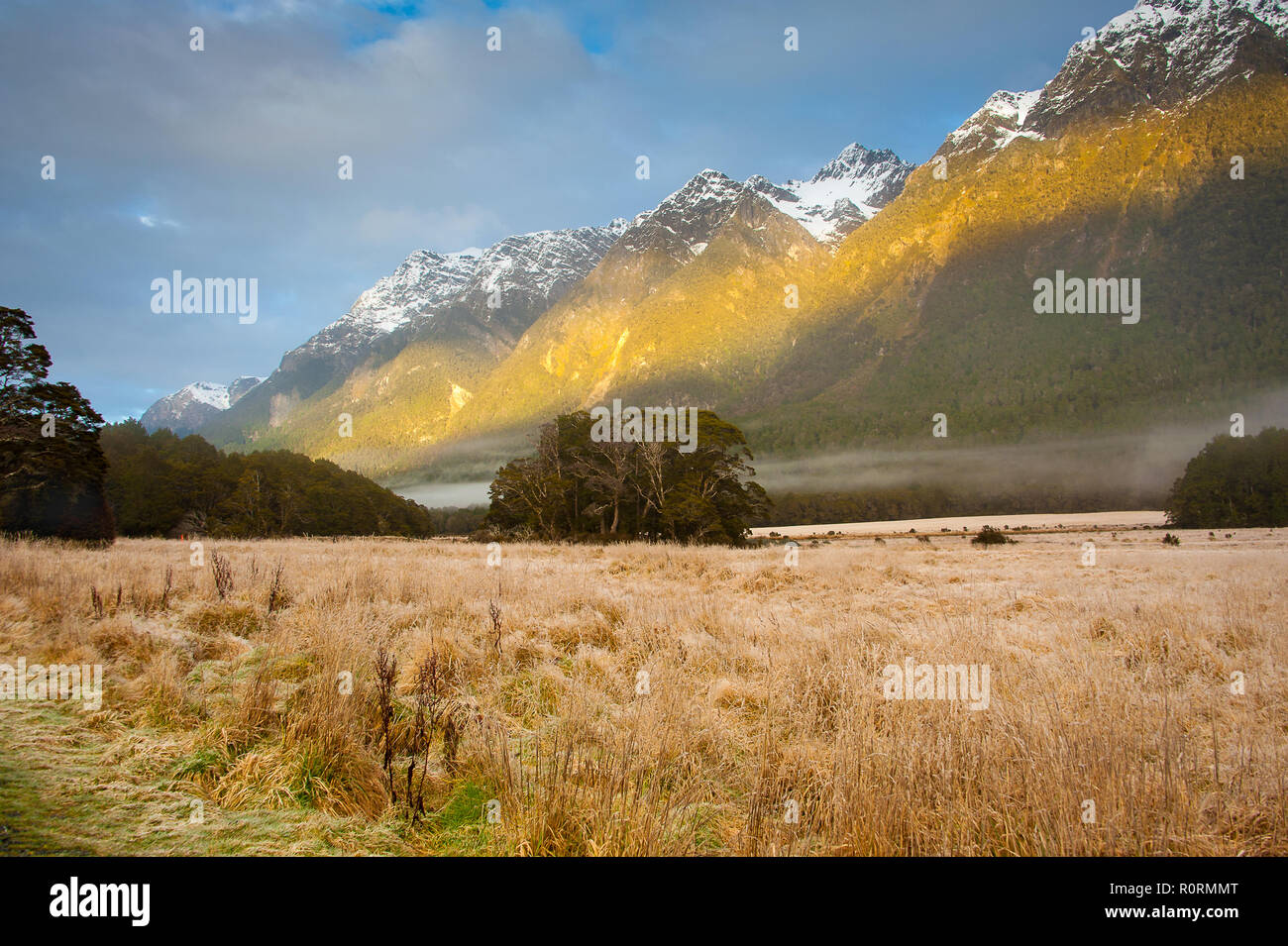 Sonnenaufgang im Fjordland, Neuseeland. Nebel Hängen über dem Tal, mit schneebedeckten Bergen und bewölkter Himmel Hintergrund. Stockfoto