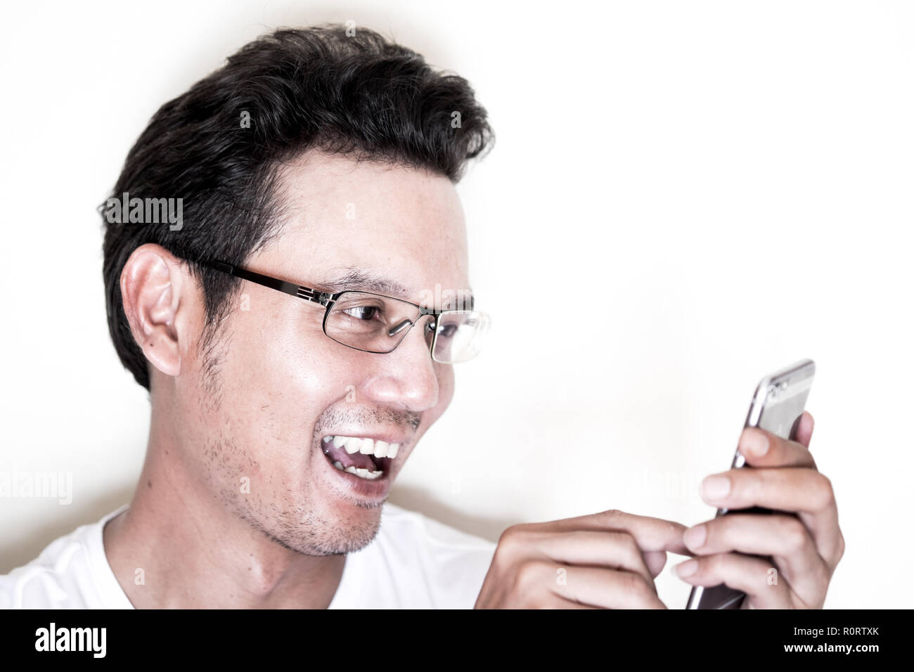 Stattliche asiatischer Mann mit Bart und lockiges Haar zu tragen Brillen für in der Nähe von sie ihr Smartphone gesichtet. Lachend und fröhlich. Stockfoto