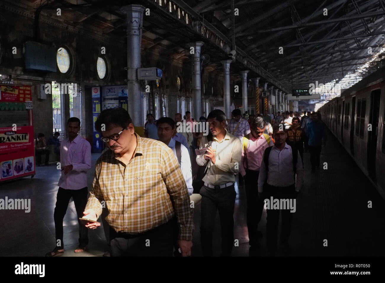 Ein Passagier ausgeschifft aus einem Nahverkehrszug in Chhatrapati Shivaji Maharaj Terminus (Csmt), Mumbai, Indien, Kontrolle auf seinem Mobiltelefon Stockfoto