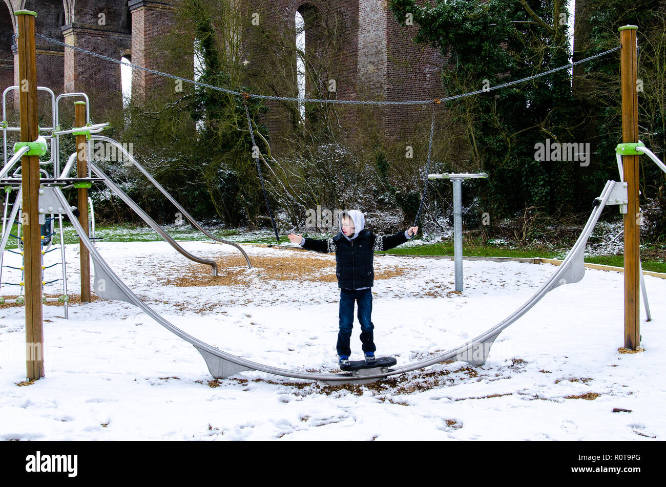 Einen kleinen Jungen mit ADHS, Autismus, Asperger Syndrom spielt in einem Park auf seinem eigenen an einem verschneiten Tag im Süden von England Stockfoto