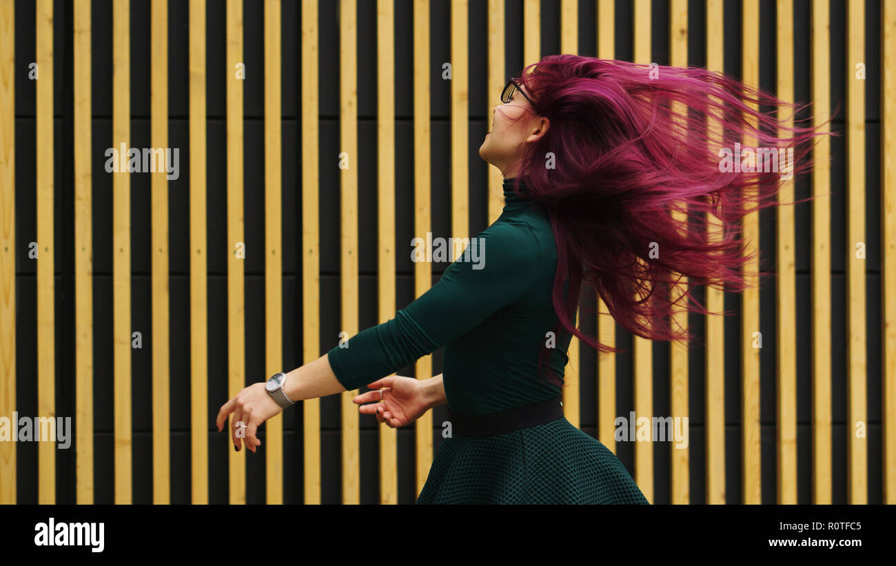 Junge Mädchen tanzen auf dem Hintergrund einer einfachen geometrischen Muster NIEDLICH. Mädchen hat Aubergine Haar in Bewegung fliegen. Sie ist in dunklem grün Kleid Stockfoto