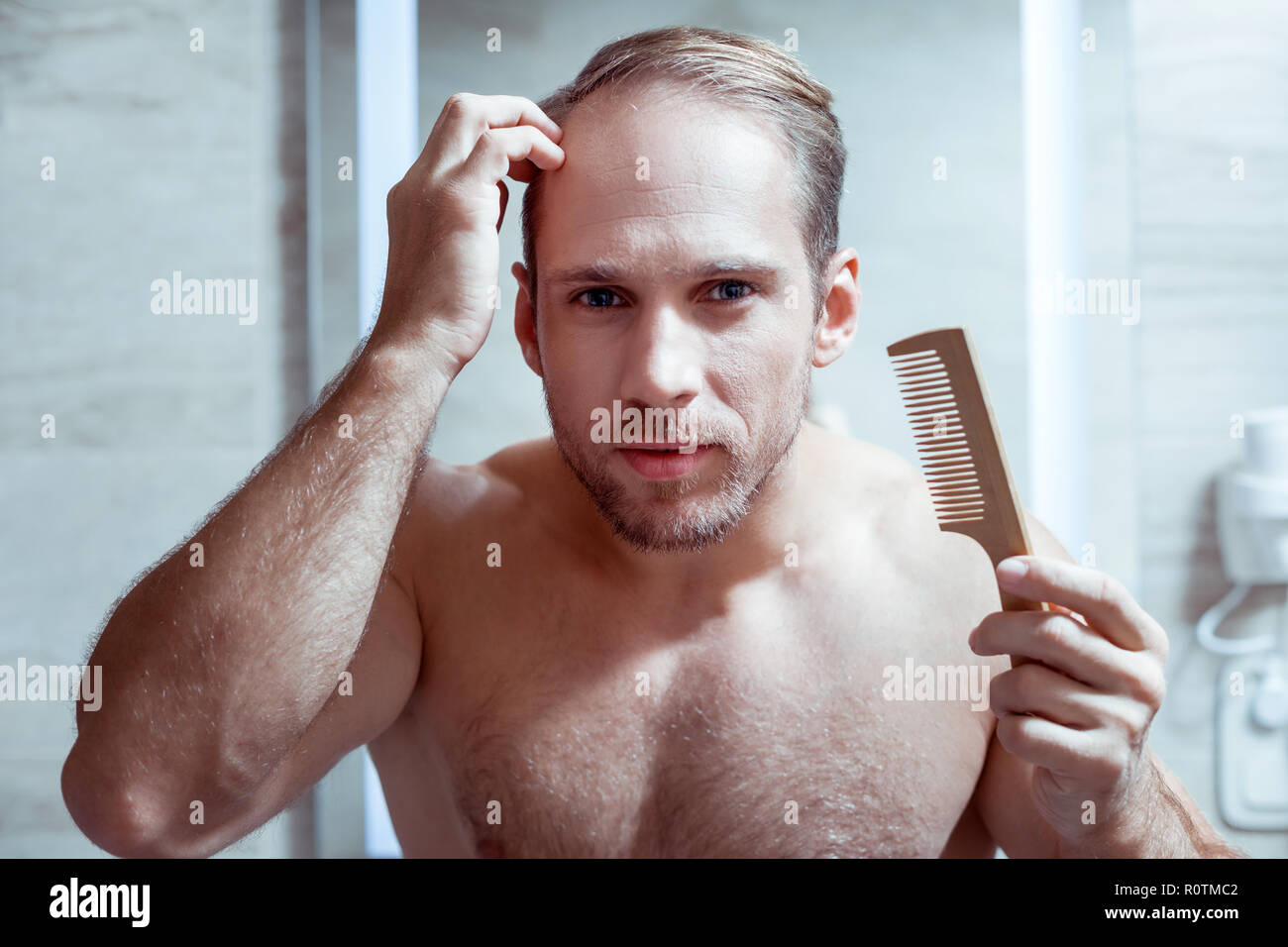 Blauäugigen Mann seine nassen Haare kämmen nach dem Waschen in der Dusche Stockfoto