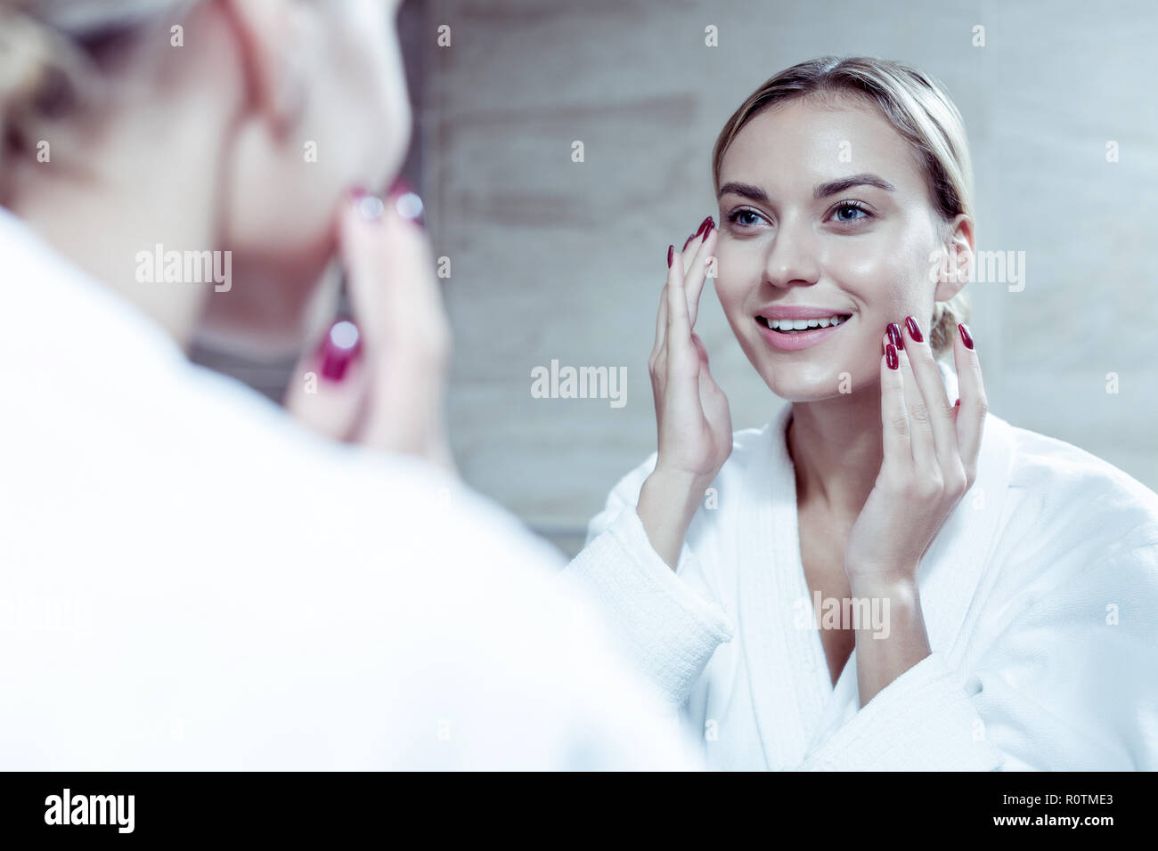 Schöne junge Frau lächelnd, während in den Spiegel schauen und mit Sahne Stockfoto