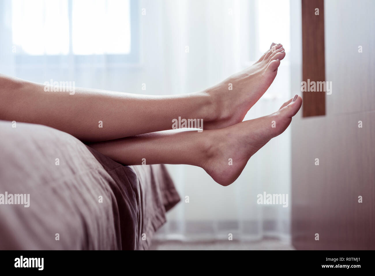 Frau mit beige Pediküre liegend auf ein schönes, großes Doppelbett im Zimmer Stockfoto