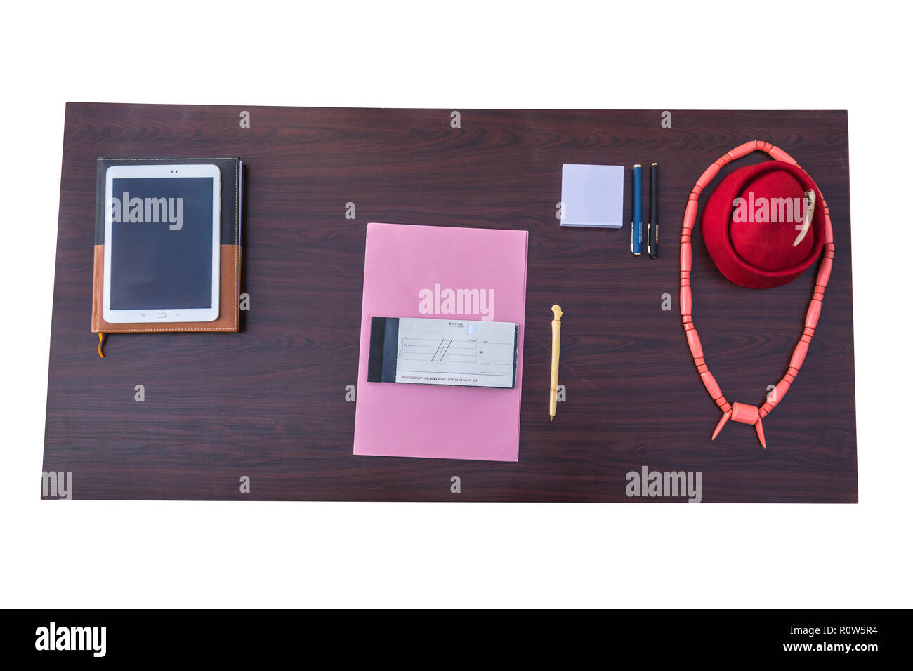 Die Tabelle, in der die afrikanischen Geschäftsmann, der seine redcap mit Federn, Perlen Halskette, jotter, rosa Datei, Holz- pen, Dokumente, Tablet- und Tagebuch. Stockfoto