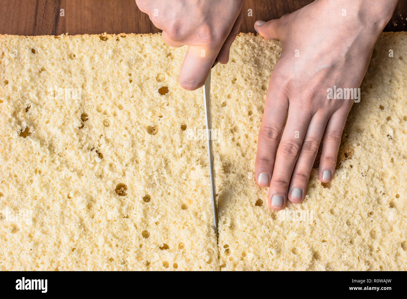 Schneiden Biskuitboden auf lagen. Vorbereitung einer Torte Kuchen, Detail der Hände und Messer, close-up Stockfoto