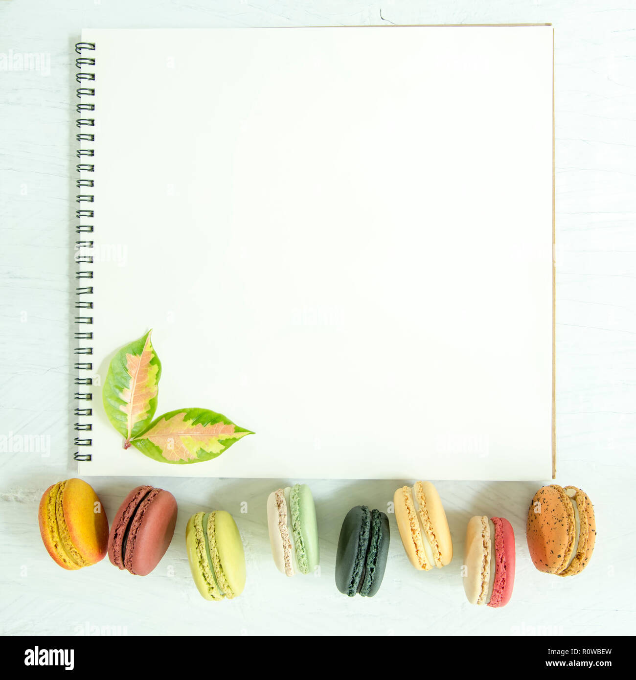 Bunte Makronen und Blätter mit leeren Seite der Offenen weißen Notebook auf dem Tisch. Stockfoto
