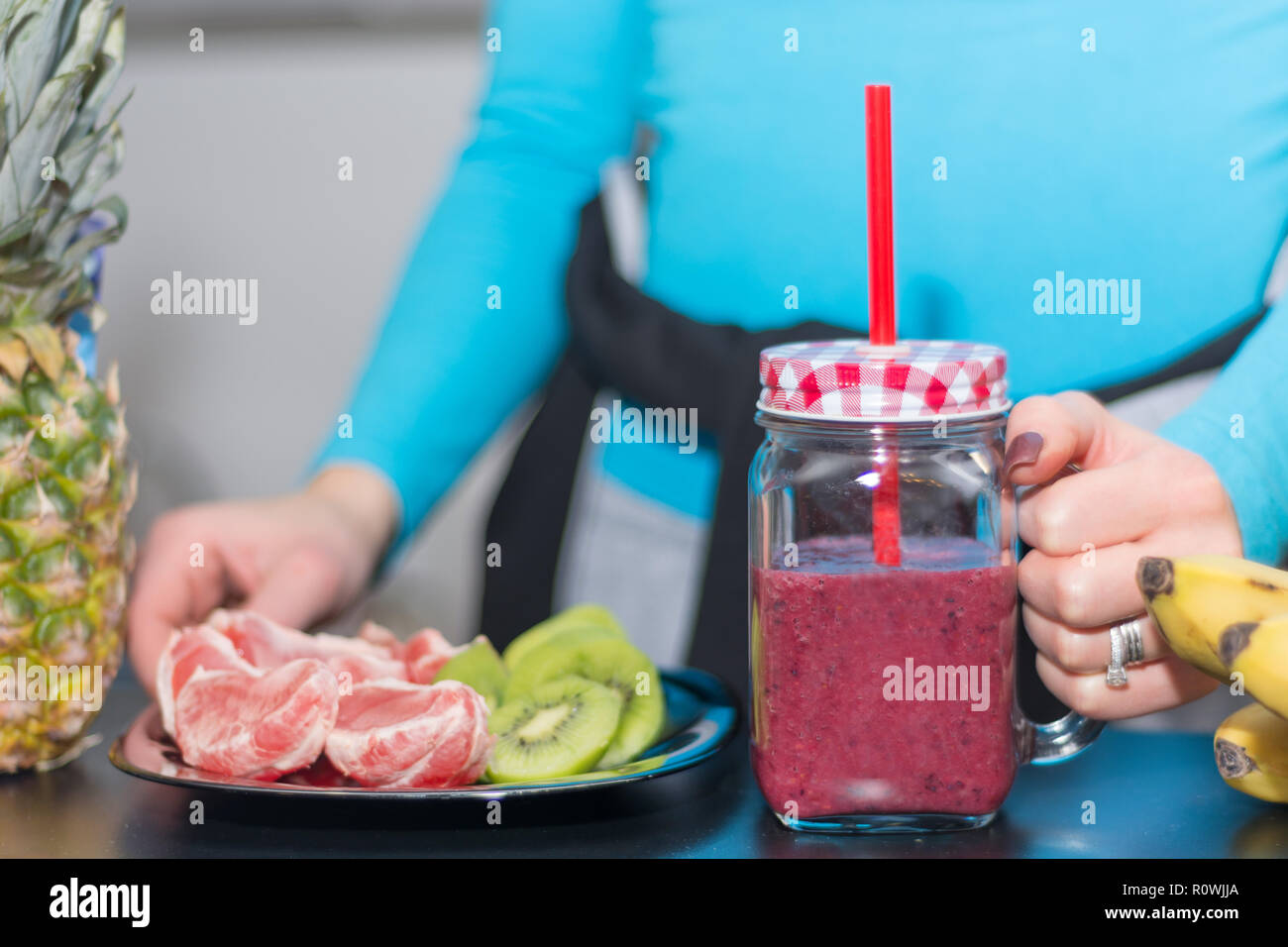 Mädchen, dass Mason jar Becher mit roten Smoothie und Platte mit geschälte Grapefruit und Kiwi Salat an Küche Schreibtisch gefüllt. Gesunde und Entgiftung essen und trinken Stockfoto