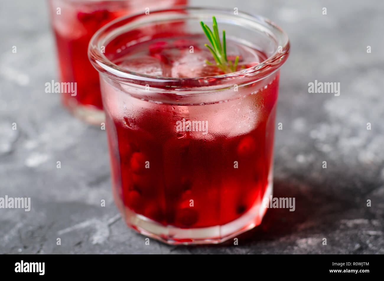Cranberry Cocktail mit Eis und Rosmarin auf grauen Hintergrund, erfrischendes Getränk Stockfoto