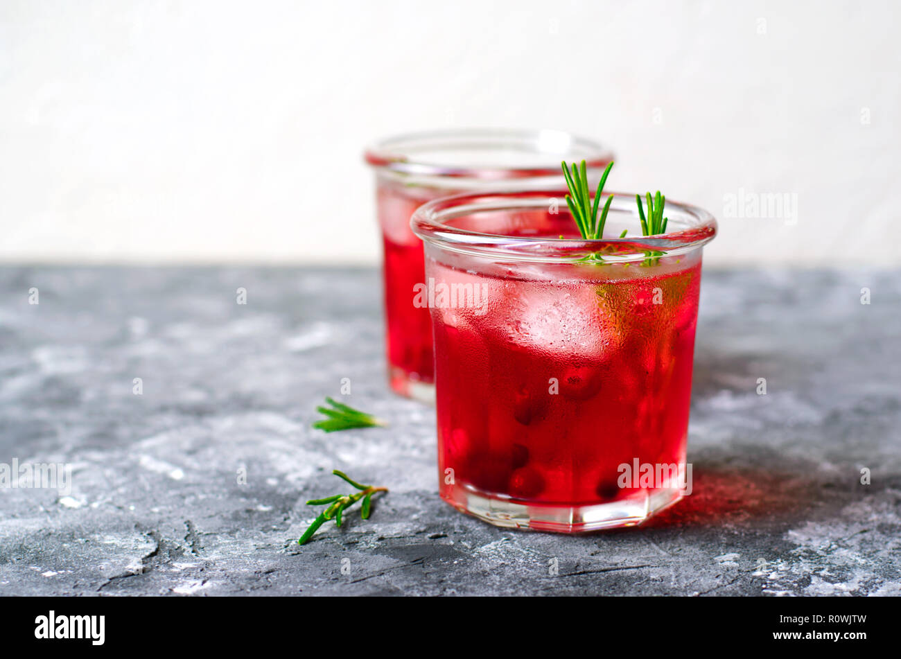 Cranberry Cocktail mit Eis und Rosmarin auf grauen Hintergrund, erfrischendes Getränk Stockfoto