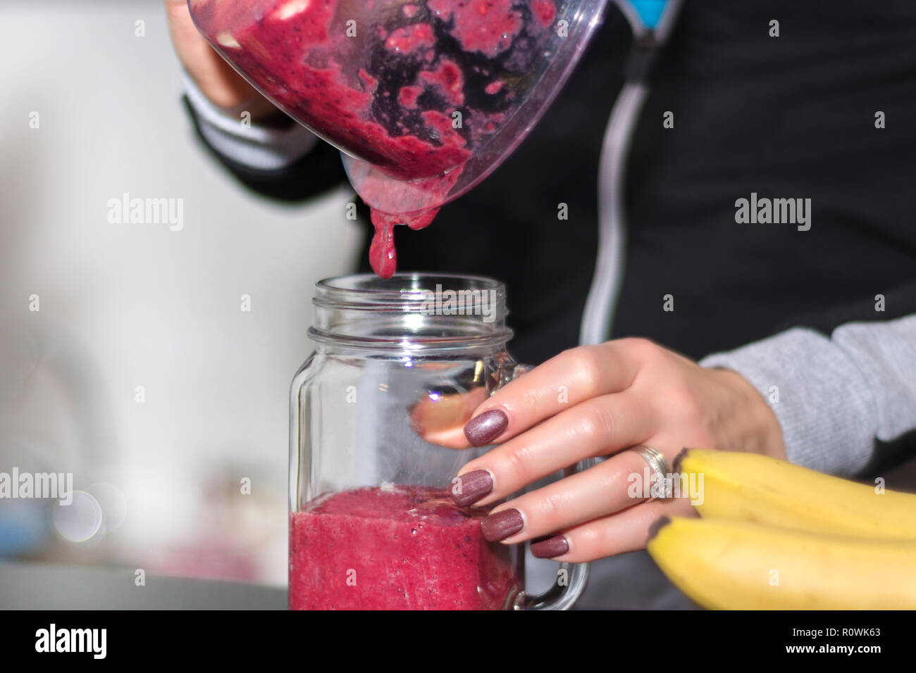 Mädchen gießt red Berry Smoothie von Blender zu Glas Glas in der Küche zu Hause. Gesunde und Entgiftung essen und trinken Konzept. Close Up, selektiver Fokus Stockfoto