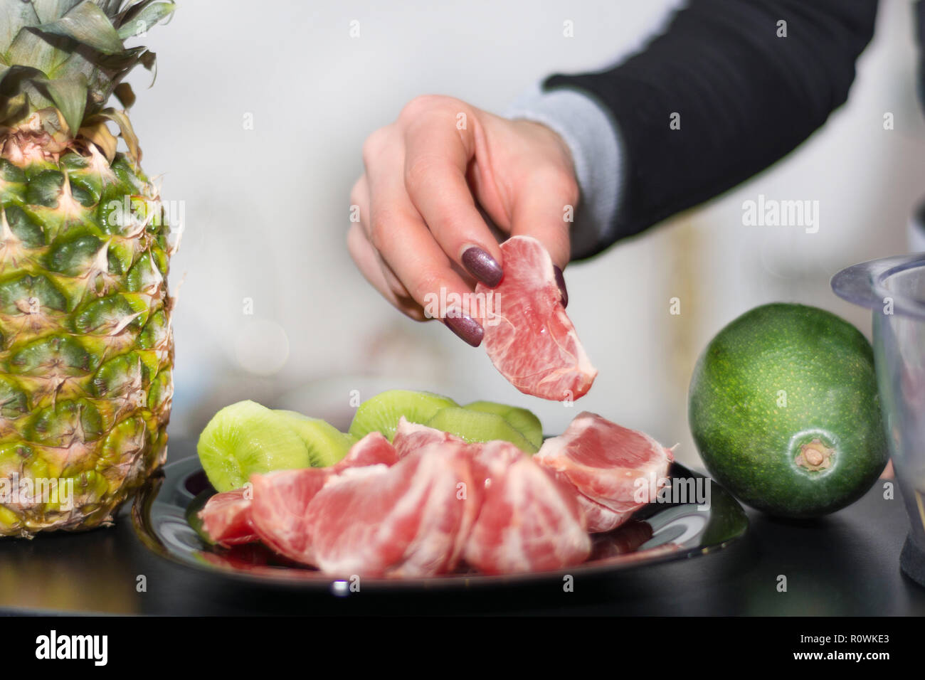 Frau Hand hält Rote geschälte Grapefruit an der Platte. Gesundes Obst Salat auf dem Schreibtisch in der Küche. Close Up, selektiver Fokus Stockfoto