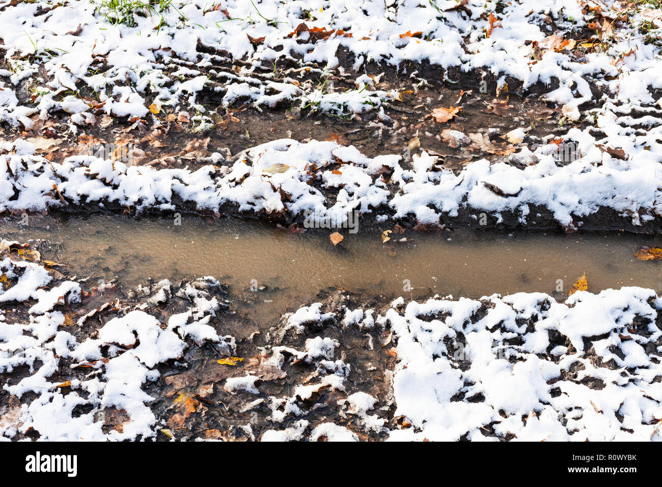 Pfütze in der schmutzige Straße mit dem ersten Schnee im Wald im kalten Herbst Tag abgedeckt Stockfoto