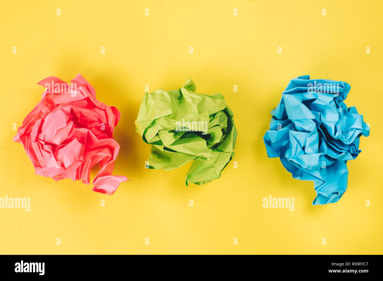 Pink, Blau und Grün zerknittertes Papier Kugeln auf gelben Hintergrund. Konzept der Idee, recyceln und Stress Stockfoto