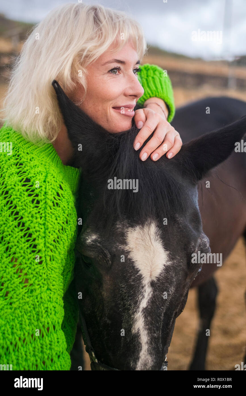 Liebe Konzept für Menschen und animlas zusammen in Glück und Freundschaft. beaitufl blonde Frau und Dark Horse im Freien malerischen Ort umarmen und lov Stockfoto