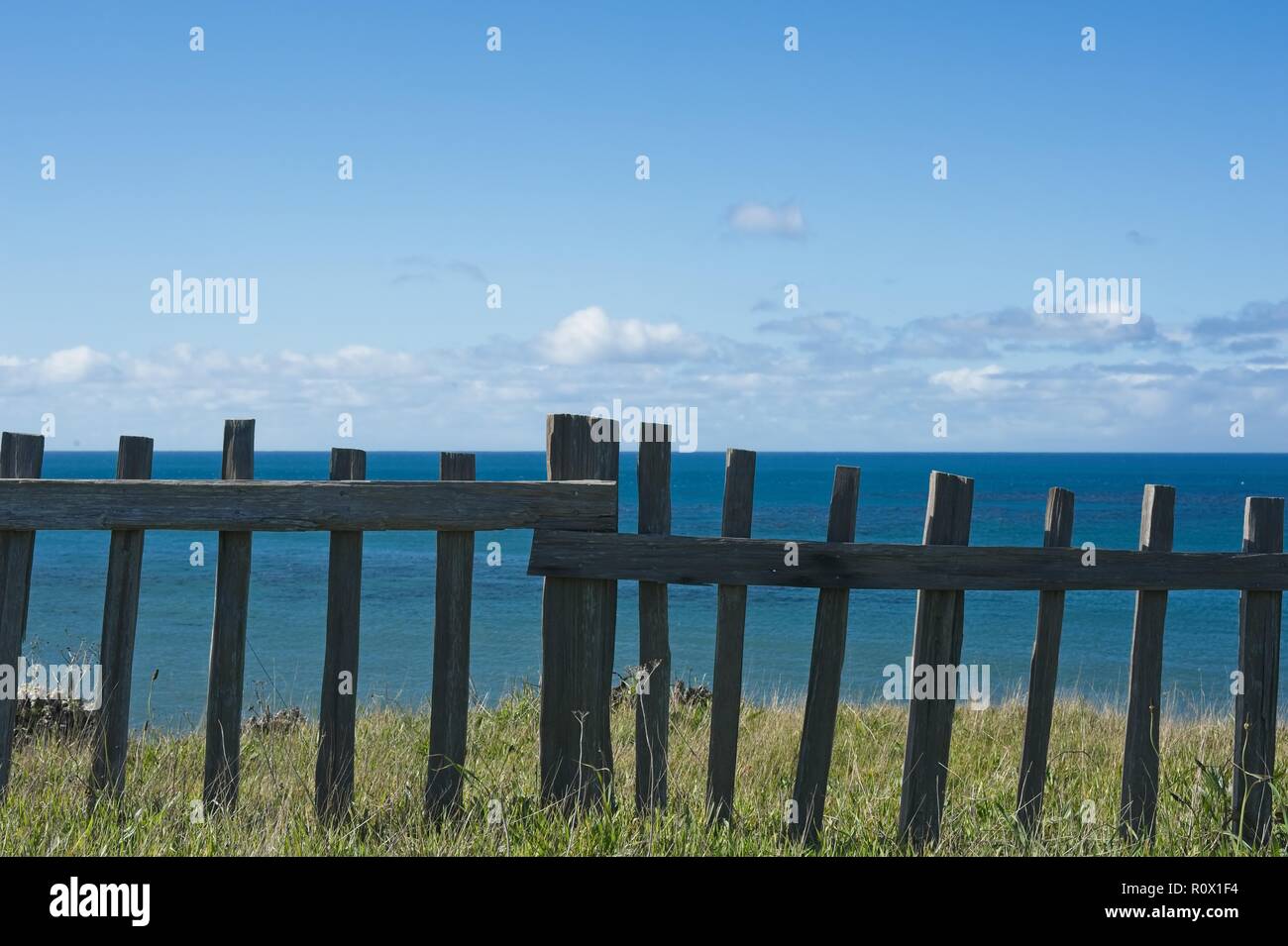 Pazifik Ansicht aus einer grasbewachsenen Hügel hinter einem hölzernen Barriere Zaun gegen einen blauen Himmel mit puffy Clouds Stockfoto