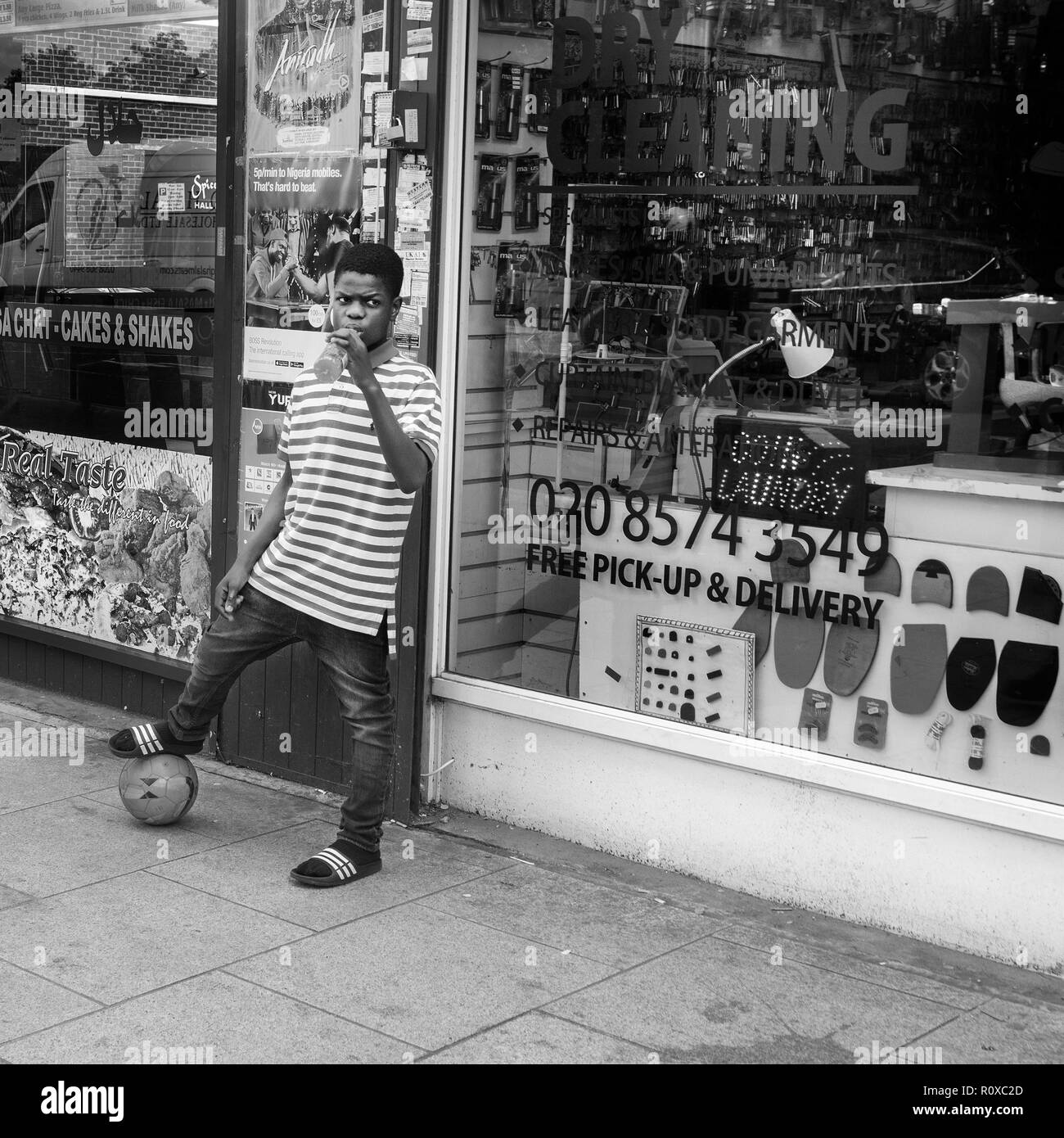Junge mit Fußball unter seinem Fuß, Getränk in der Hand, draußen auf der Straße eine chemische Reinigung Shop, Southwark broadway London UK Stockfoto