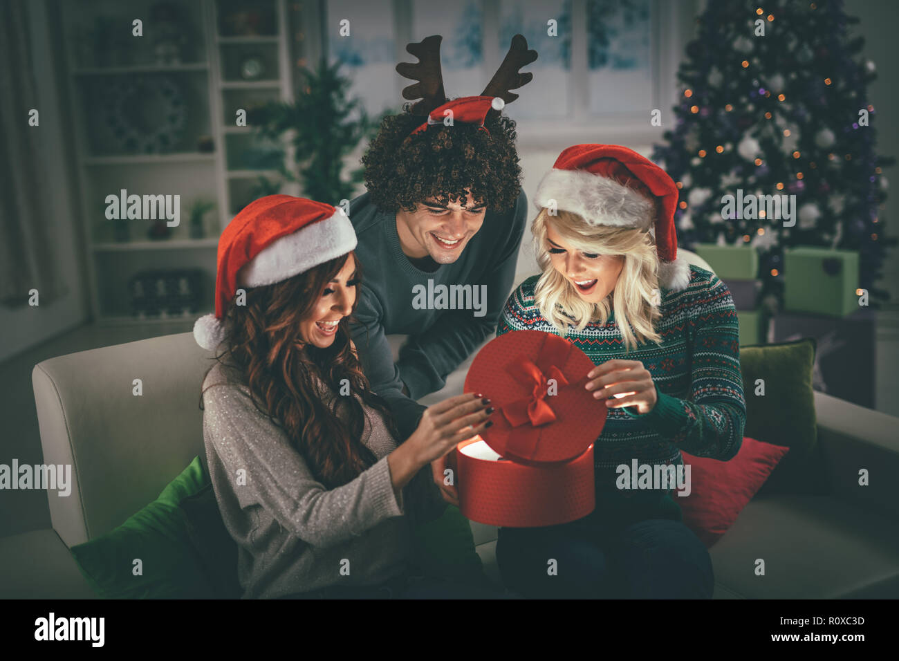 Fröhliche schöne junge Freunde Weihnachten zu Hause genießen, Geschenk und überraschend, was drin ist. Stockfoto
