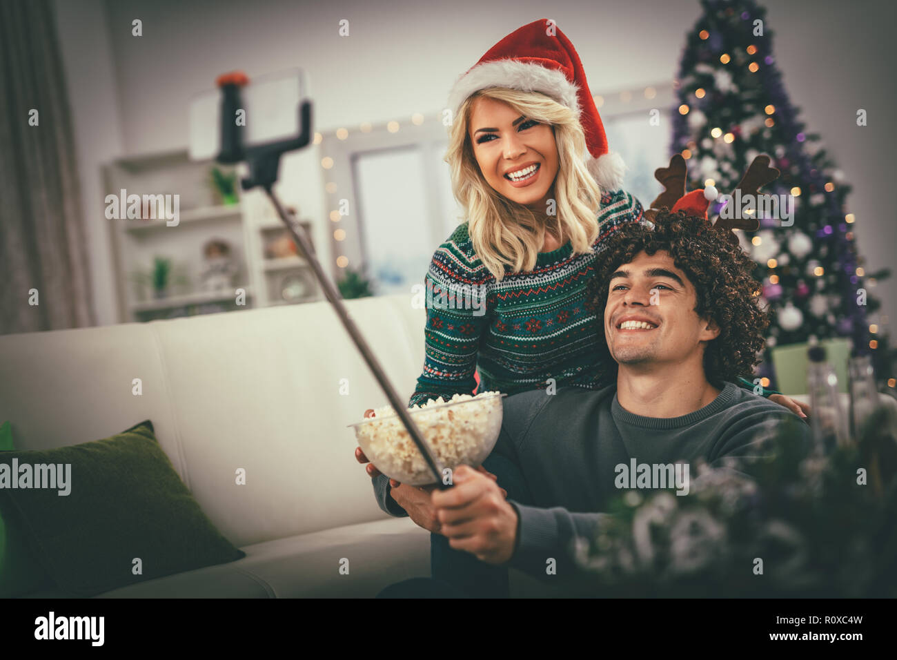 Paar in der gemütlichen warmen Pullover auf ein Weihnachten - Neujahr, lächeln und Spaß unter selfie und essen Popcorn. Stockfoto