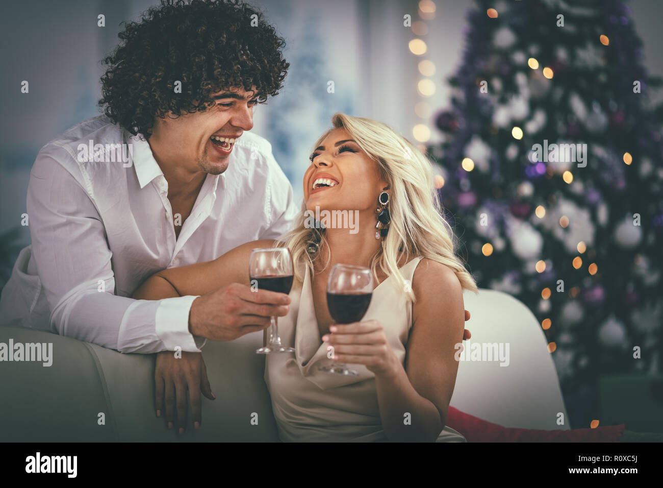 Junges Paar Weihnachten zu Hause feiern. Entspannen Sie sich mit einem Glas Rotwein, mit Decke auf dem Sofa in einer Wohnung abgedeckt. Stockfoto