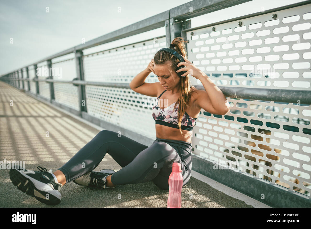 Junge fitness Frau ruht sich nach harten Training auf dem River Bridge, Ihr Kopfhörer und eine Flasche Wasser, in der Nähe von ihr ist. Stockfoto