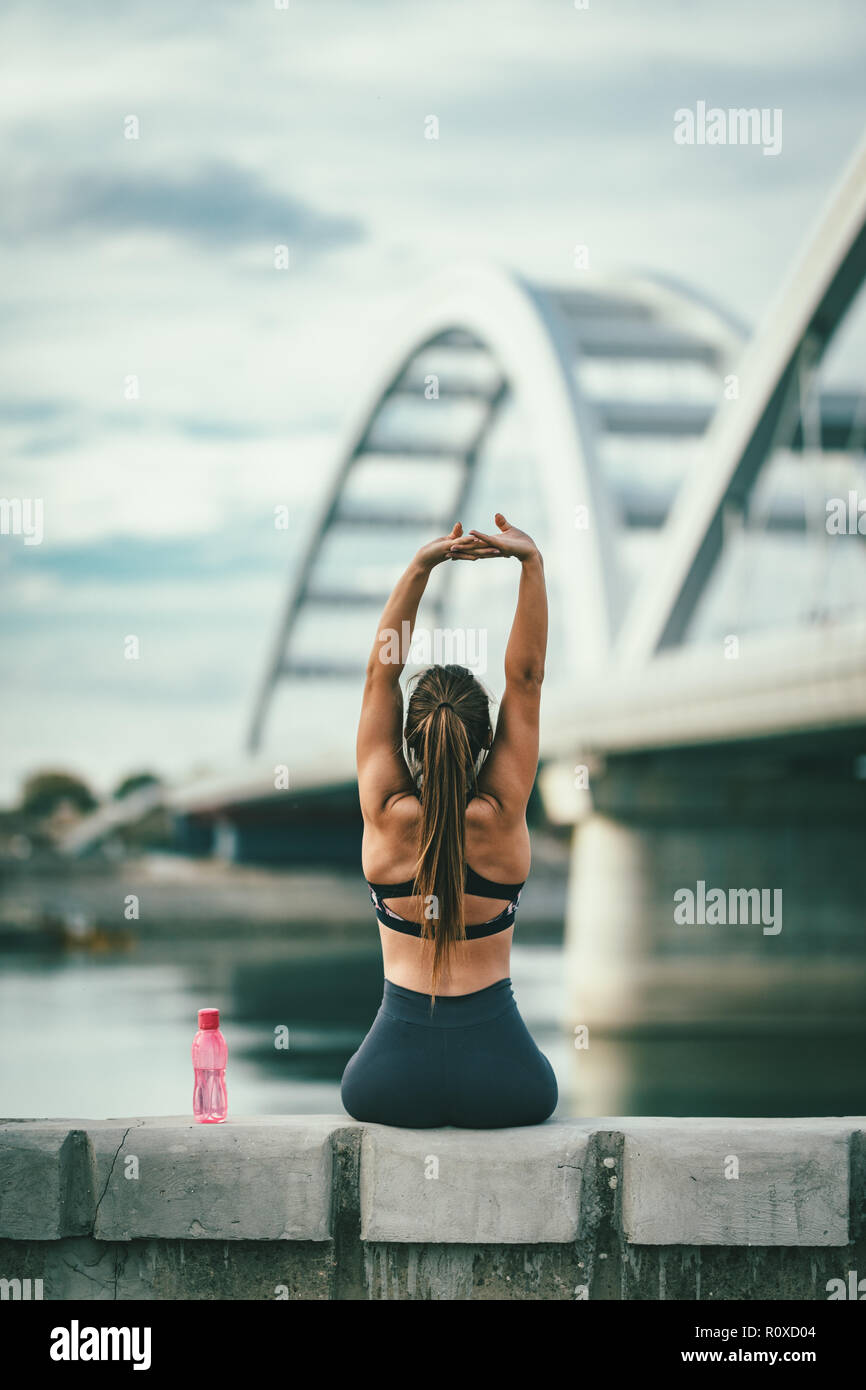 Junge fitness Frau ruht und Stretching nach harten training durch die Brücke über den Fluss, Trinkwasser. Stockfoto