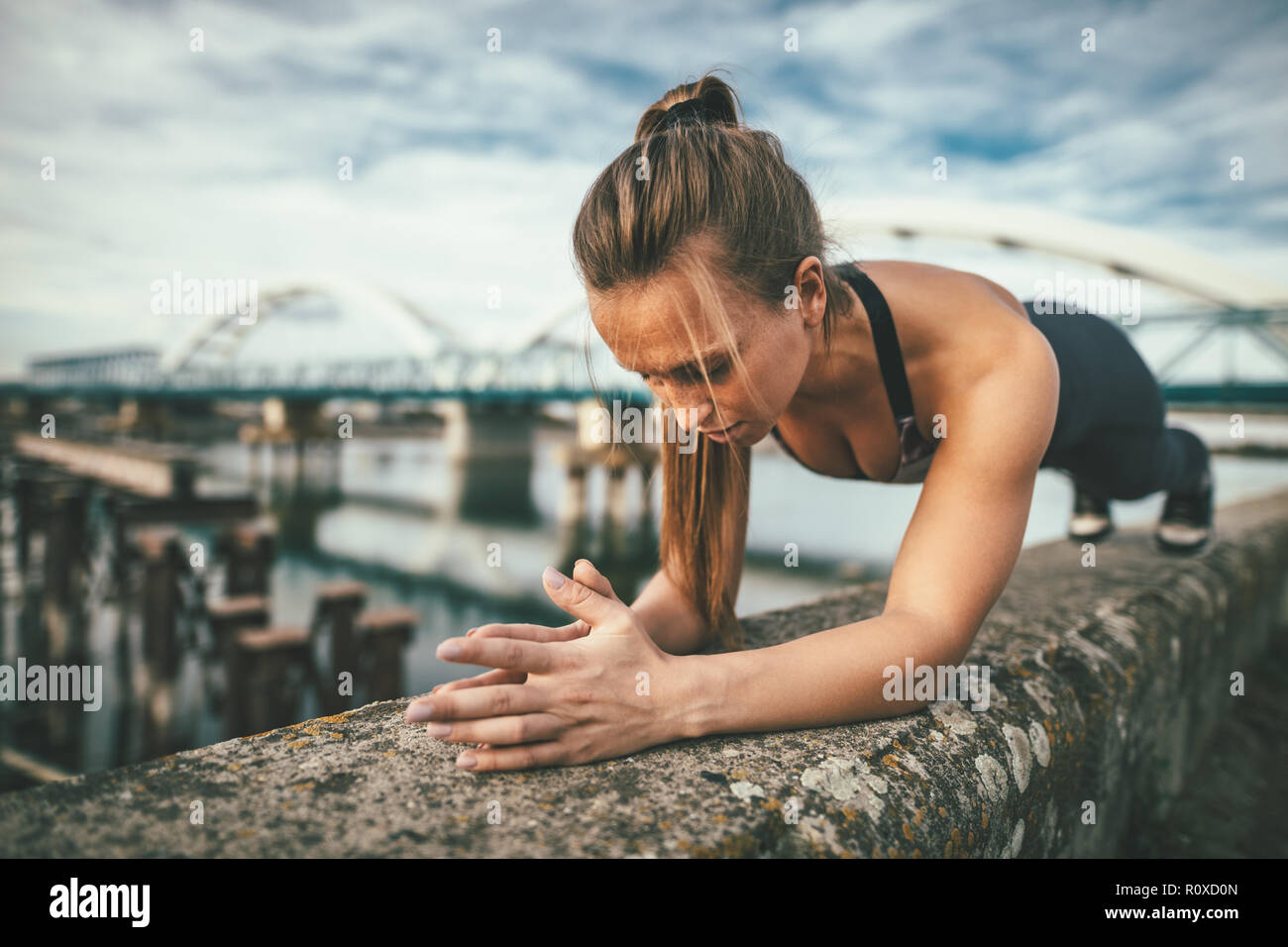 Young Sport Frau tun plank Übung auf der Wand während outdoor Cross Training durch den Fluss fokussiert. Stockfoto