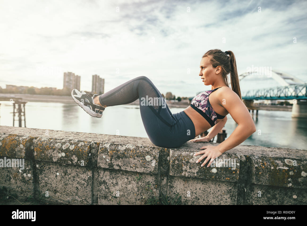 Schwerpunkt junge Sportart Frau tun, Sit-up Übungen an der Wand während outdoor Cross Training durch den Fluss. Stockfoto