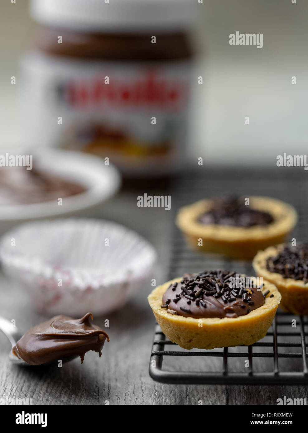 Nutella Törtchen mit Schokolade besprüht, auf einer Unterlage Rack mit Nutella im Hintergrund Stockfoto
