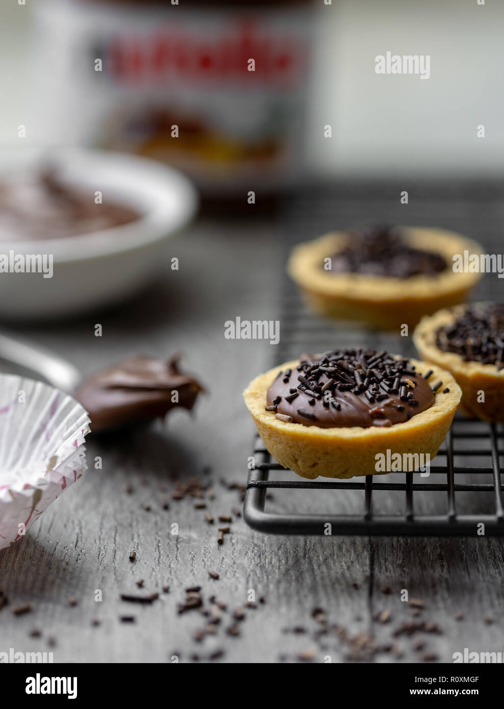 Nutella Törtchen mit Schokolade besprüht, auf einer Unterlage Rack mit Nutella im Hintergrund Stockfoto