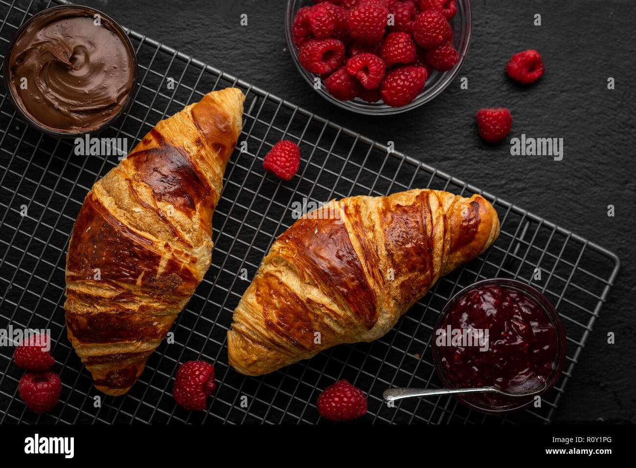 Croissants umgeben mit Himbeeren, Himbeer Marmelade und Nutella über Kopf geschossen Stockfoto