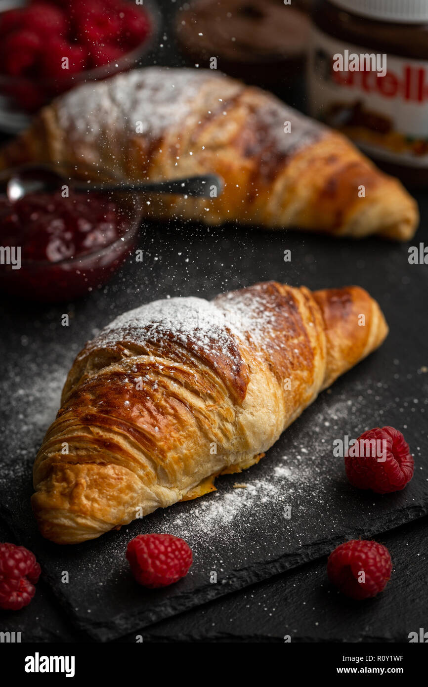 Croissants mit Puderzucker bestäubt, umgeben mit Himbeeren, Himbeer Marmelade und Nutella Stockfoto