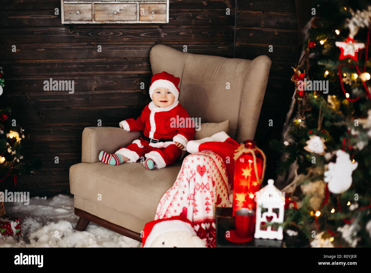 Little Santa boy in Red Suite sitzen in den grossen Sessel in der Nähe der Weihnachtsbaum. Stockfoto