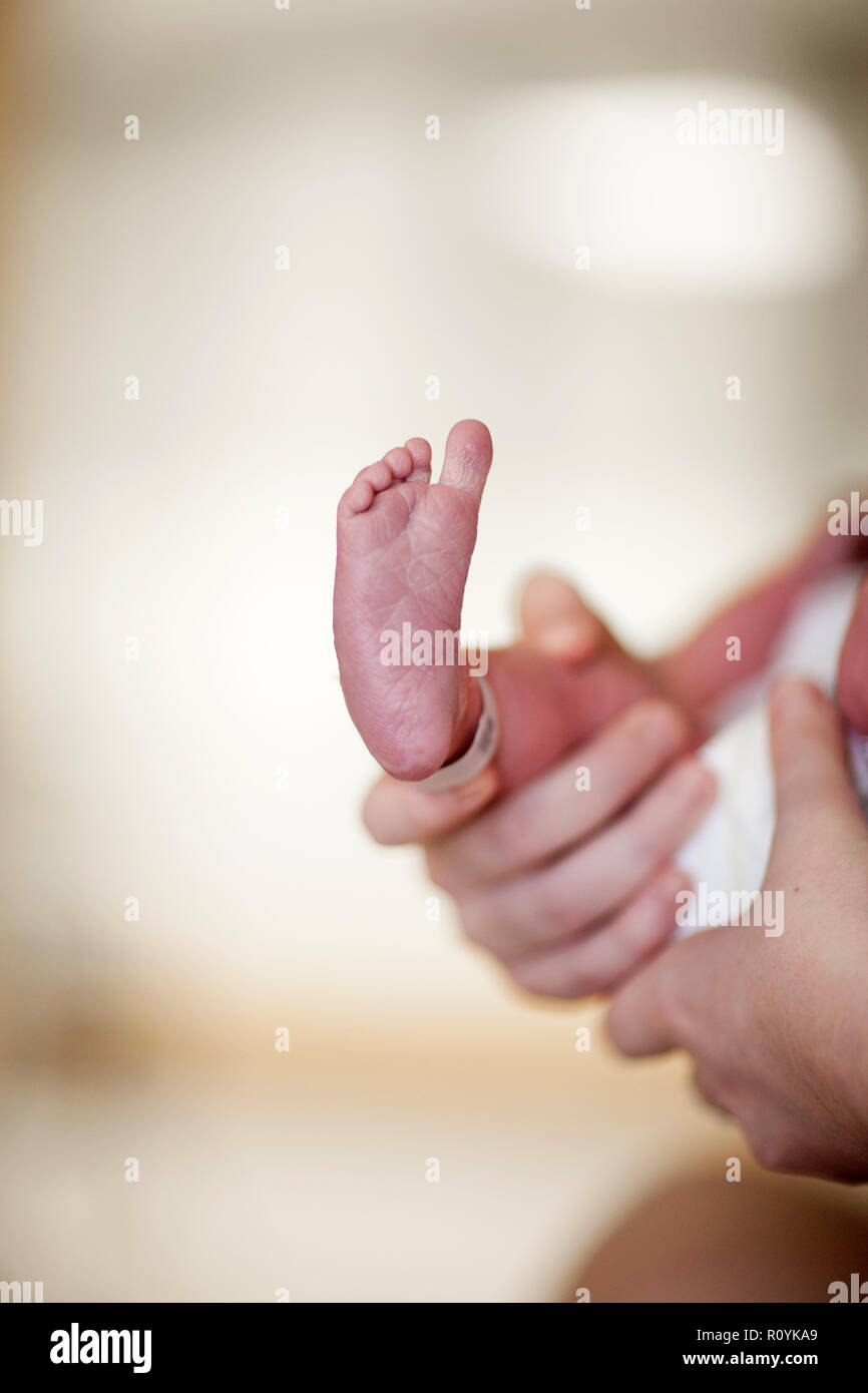 In der Nähe der Unterseite des Neugeborenen Fuß mit dem Krankenhaus Identifikation Band noch beigefügt, die Mutter hielt Stockfoto