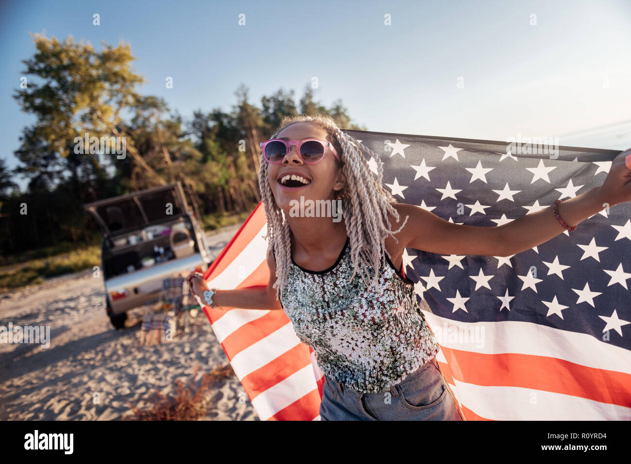 Strahlende Frau mit Dreadlocks holding Amerika Flagge unterwegs Stockfoto
