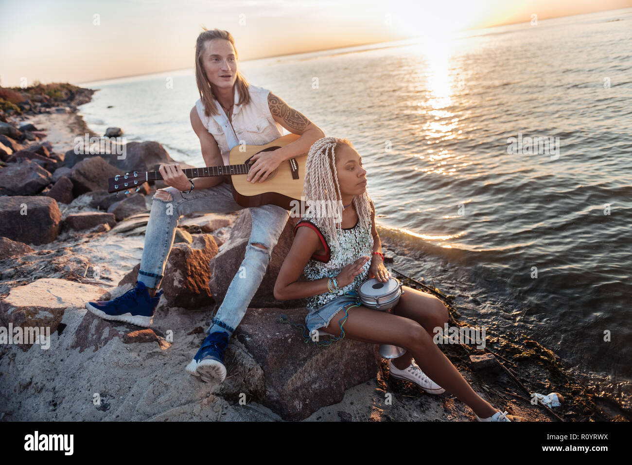 Inspiriert Musiker sitzen auf den Felsen in der Nähe von Meer und spielen Lieblingsmelodie Stockfoto