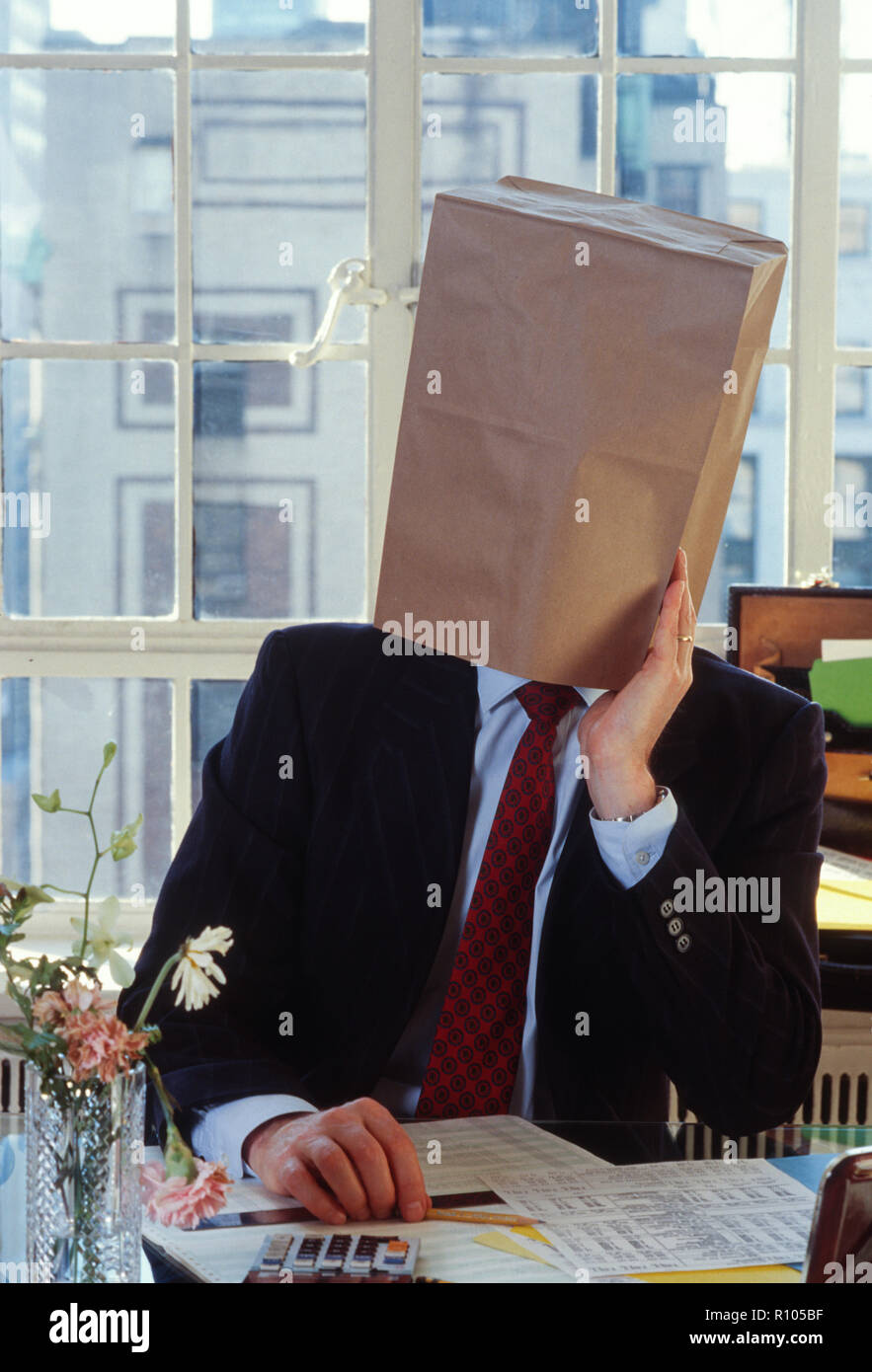 Geschäftsmann mit einem leeren braunen Papiertüte über dem Kopf sitzt am Schreibtisch, USA Stockfoto