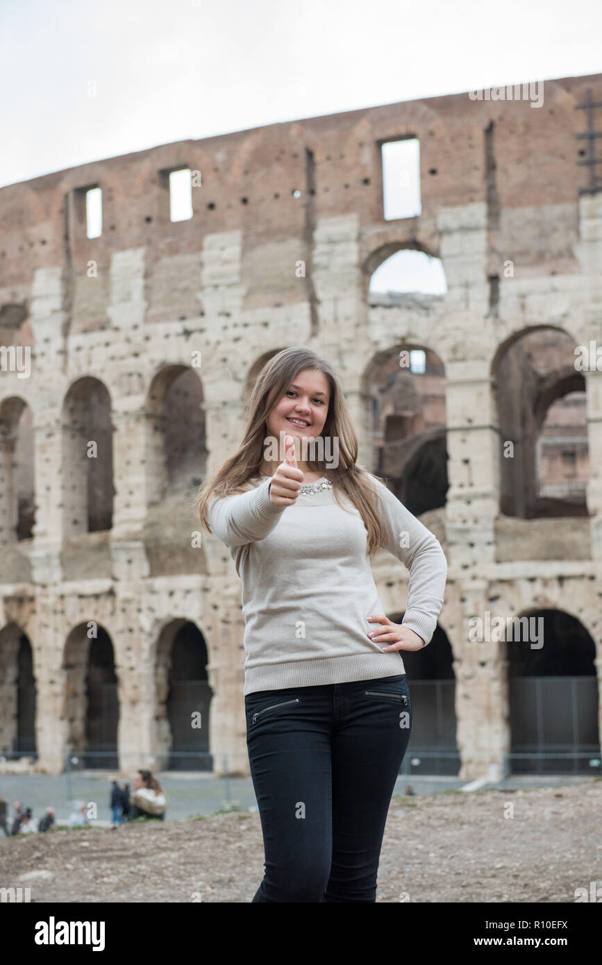 Lächelnde Mädchen tragen weiße Pullover vor dem Kolosseum, Rom, Italien, hält Daumen hoch Stockfoto