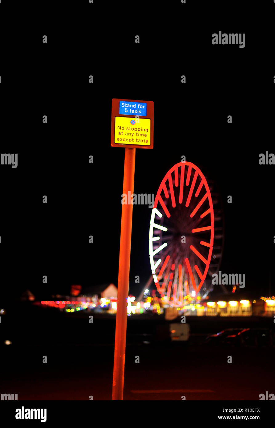Schild mit Taxistand oben am Metallpfosten und Riesenrad am Central Pier nachts während der jährlichen Blackpool-Beleuchtung Stockfoto