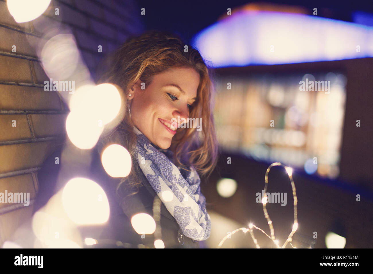 Junge Frau auf der Suche nach Lichterketten im Freien im Winter in der Stadt Stockfoto