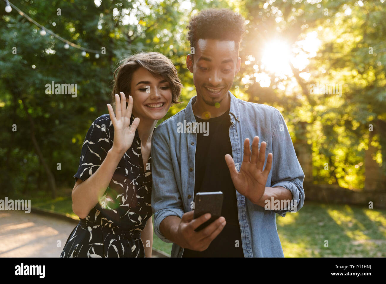 Happy multiethnischen Paar im Park, winkende Hände zu Mobiltelefon Stockfoto