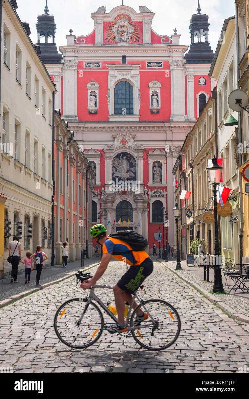 Reisen Fahrrad, eine männliche Radfahrer reiten sein Fahrrad durch Posen in Polen Blicke auf die barocke Fassade der Pfarrkirche des hl. Stanislaus. Stockfoto