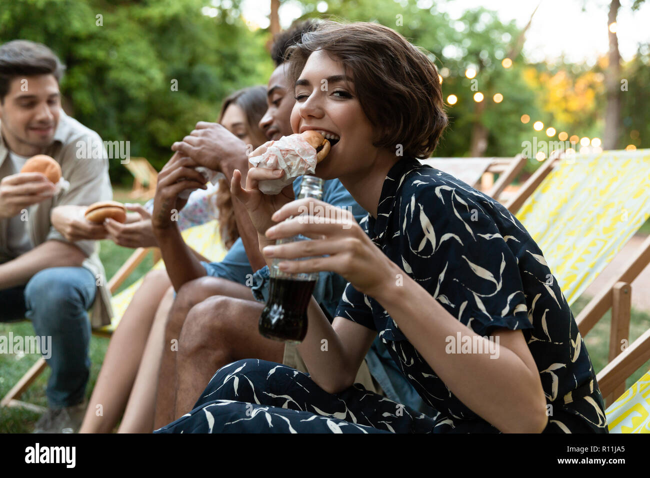 Bild der glücklichen jungen Freunde Party draußen im Park Spaß Burger essen. Stockfoto