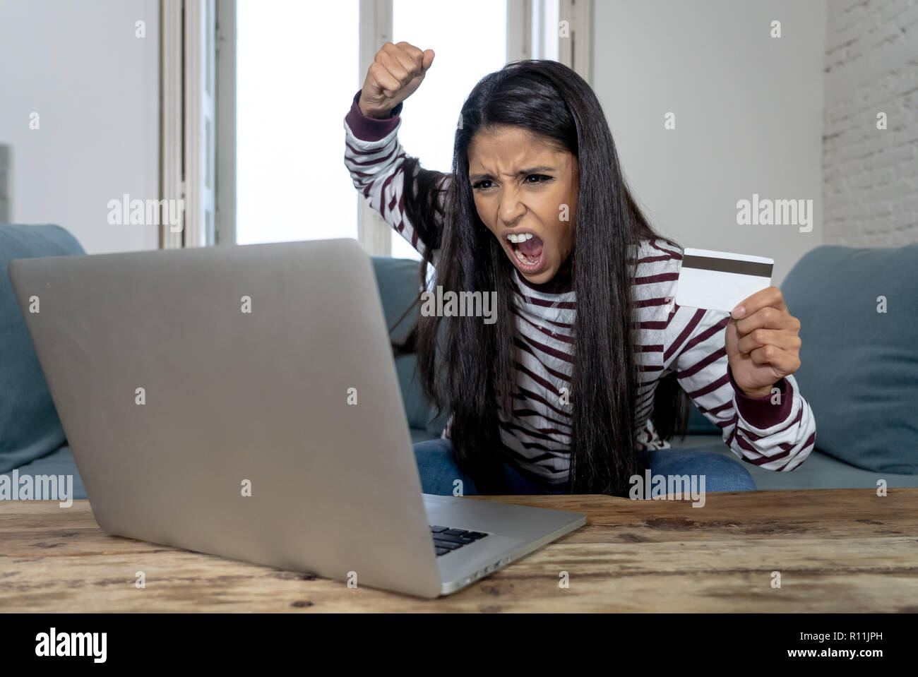 Attraktive junge Latin Frau verzweifelt und wütend mit Kreditkarte und Laptop Standortwahl auf dem Sofa zu Hause in der Kreditkarte Probleme Schulden online Zahlung online Stockfoto
