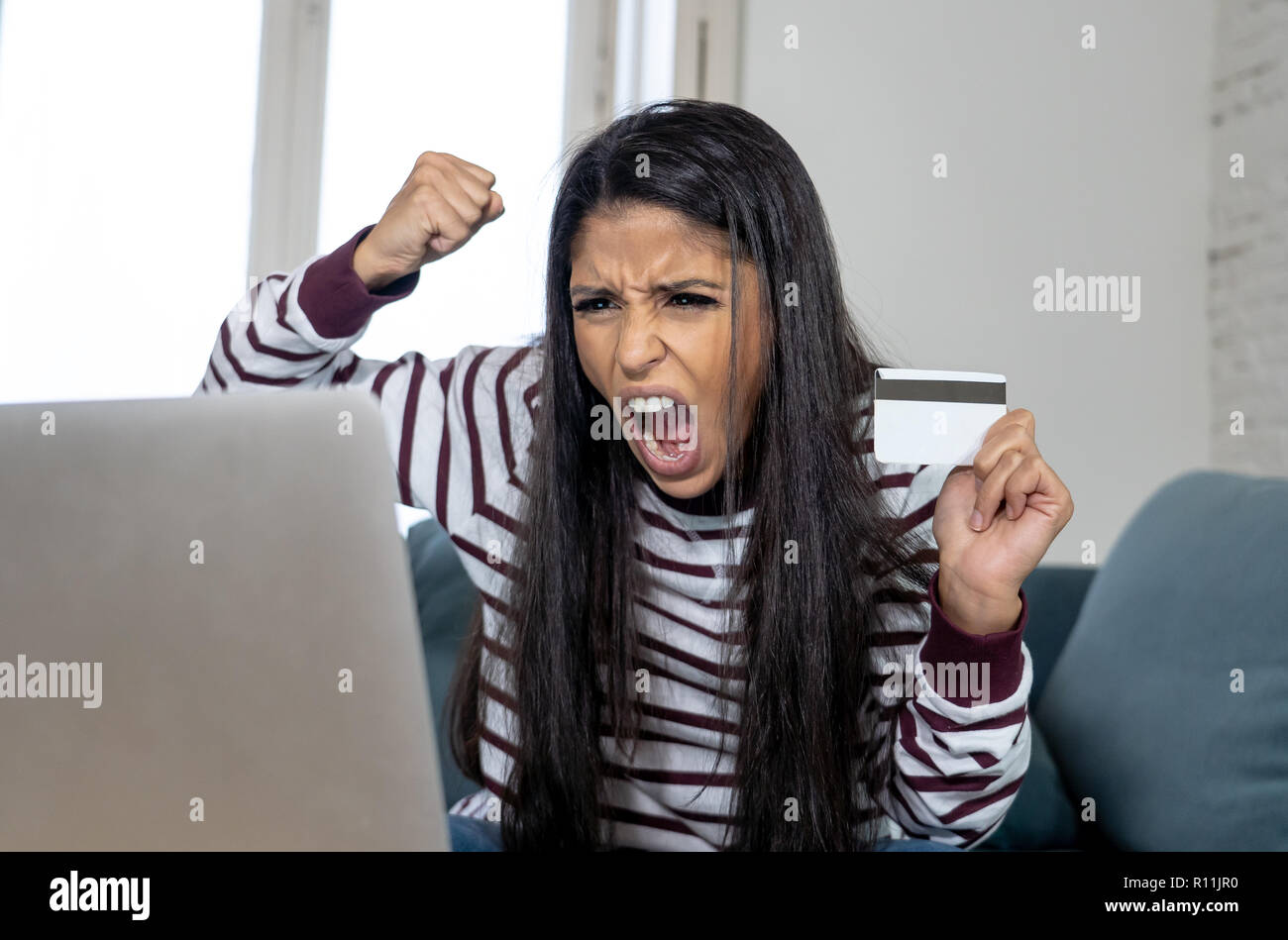 Attraktive junge Latin Frau verzweifelt und wütend mit Kreditkarte und Laptop Standortwahl auf dem Sofa zu Hause in der Kreditkarte Probleme Schulden online Zahlung online Stockfoto
