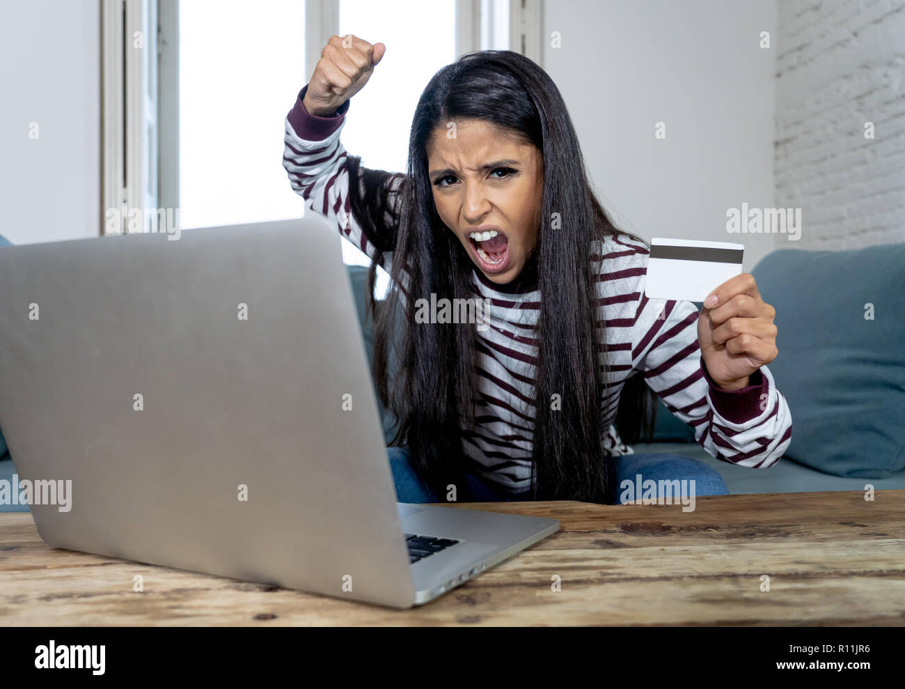 Attraktive junge Latin Frau verzweifelt und wütend mit Kreditkarte und Laptop Standortwahl auf dem Sofa zu Hause in der Kreditkarte Probleme Schulden online Zahlung online Stockfoto