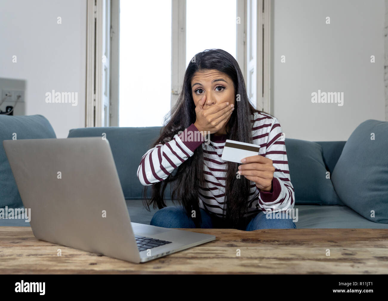 Attraktive junge Latin Frau verzweifelt und wütend mit Kreditkarte und Laptop Standortwahl auf dem Sofa zu Hause in der Kreditkarte Probleme Schulden online Zahlung online Stockfoto