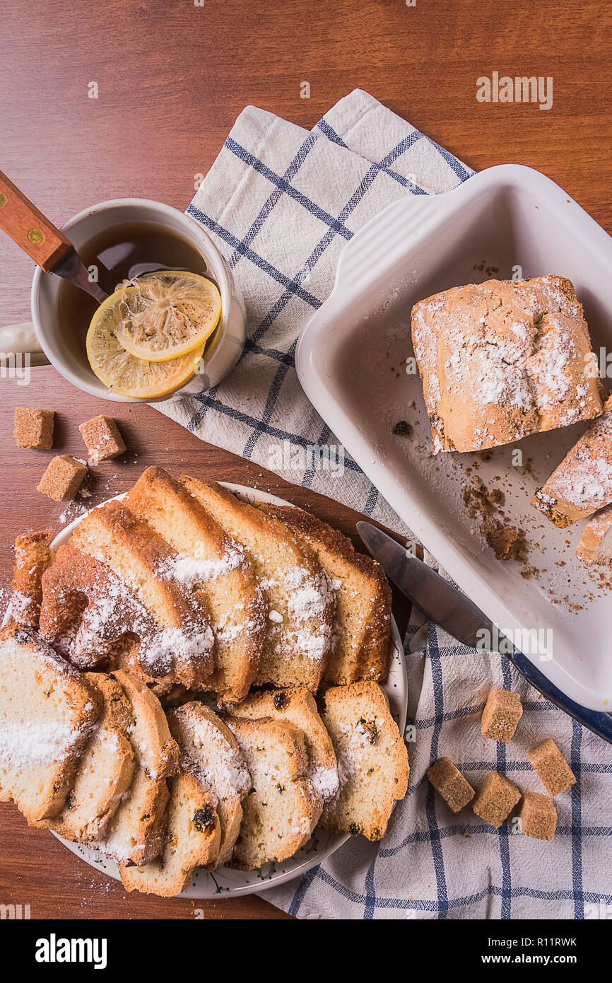 Flach auf Stück hausgemachten Kuchen mit Zucker Pulver und eine Tasse Tee mit Zitrone, über Holz- Hintergrund. Stockfoto